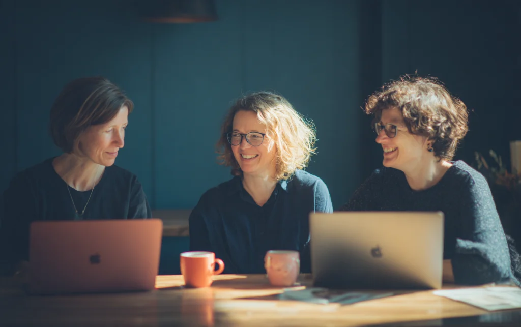 Drei Lehrpersonen vergleichen am Tisch Ergebnisse auf ihren Laptops